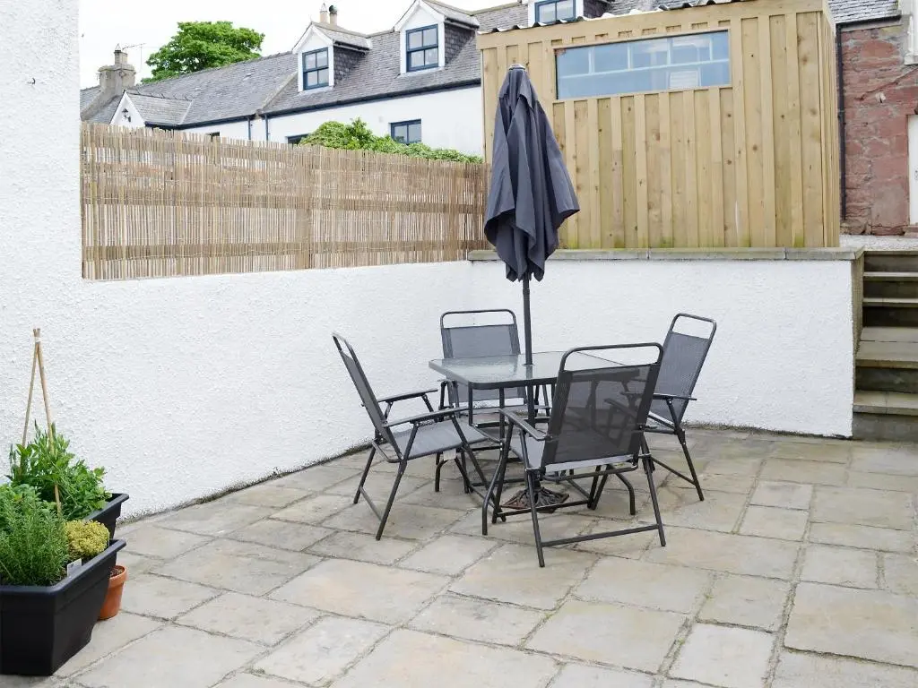 a patio with a table and chairs and an umbrella at Rosslyn Cottage in Portmahomack
