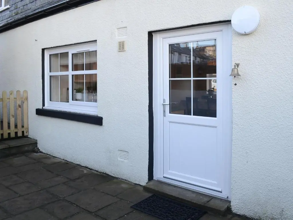 a white door on a white building with two windows at Rosslyn Cottage in Portmahomack