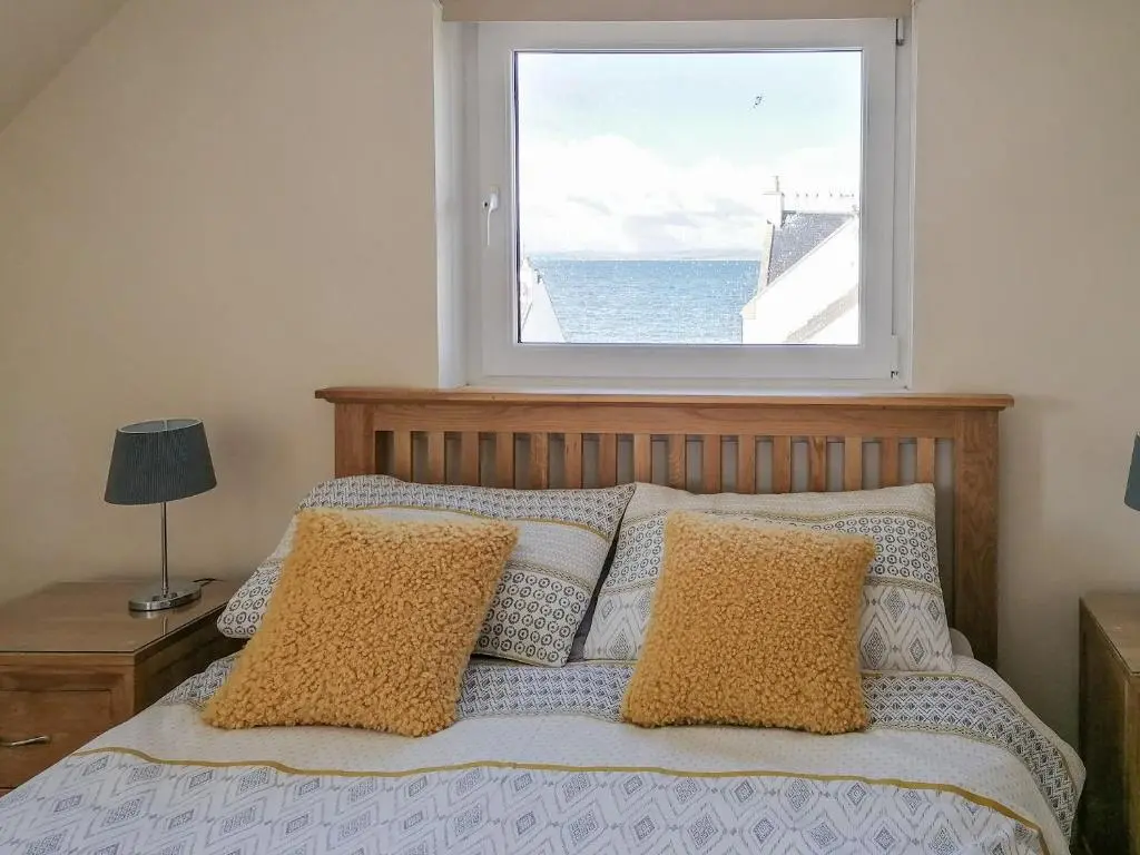 a bedroom with a bed with a large window at Rosslyn Cottage in Portmahomack