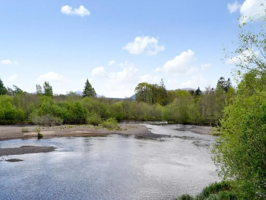 a river in a field with trees and bushes at The Pines in Aviemore