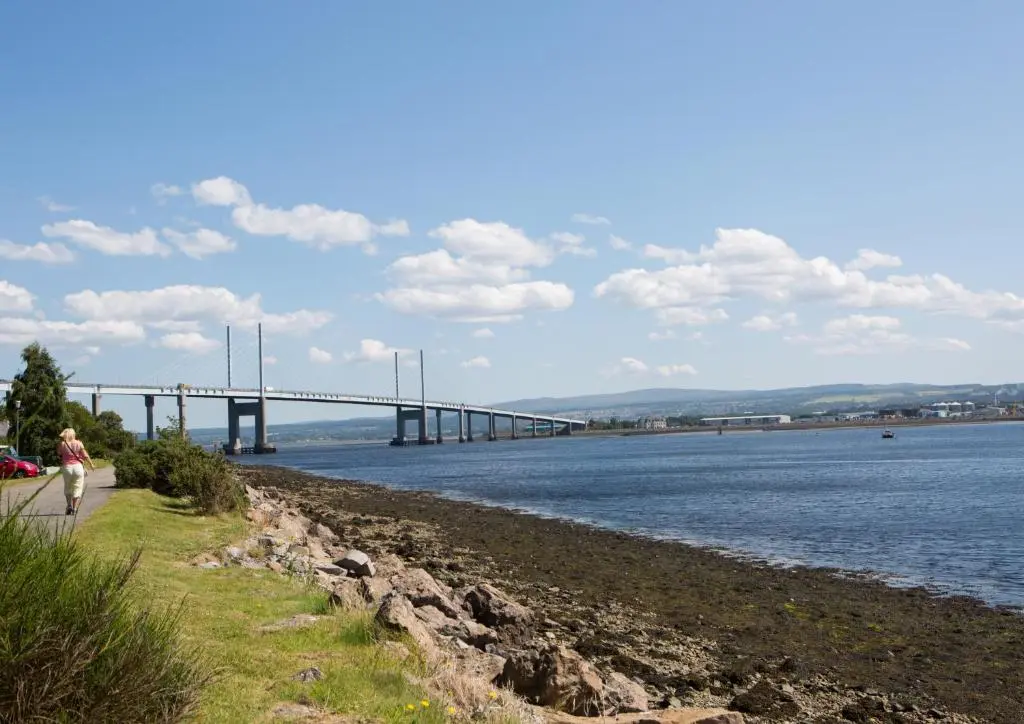 a woman walking along the shore of a river with a bridge at Shore View Cottage in Inverness