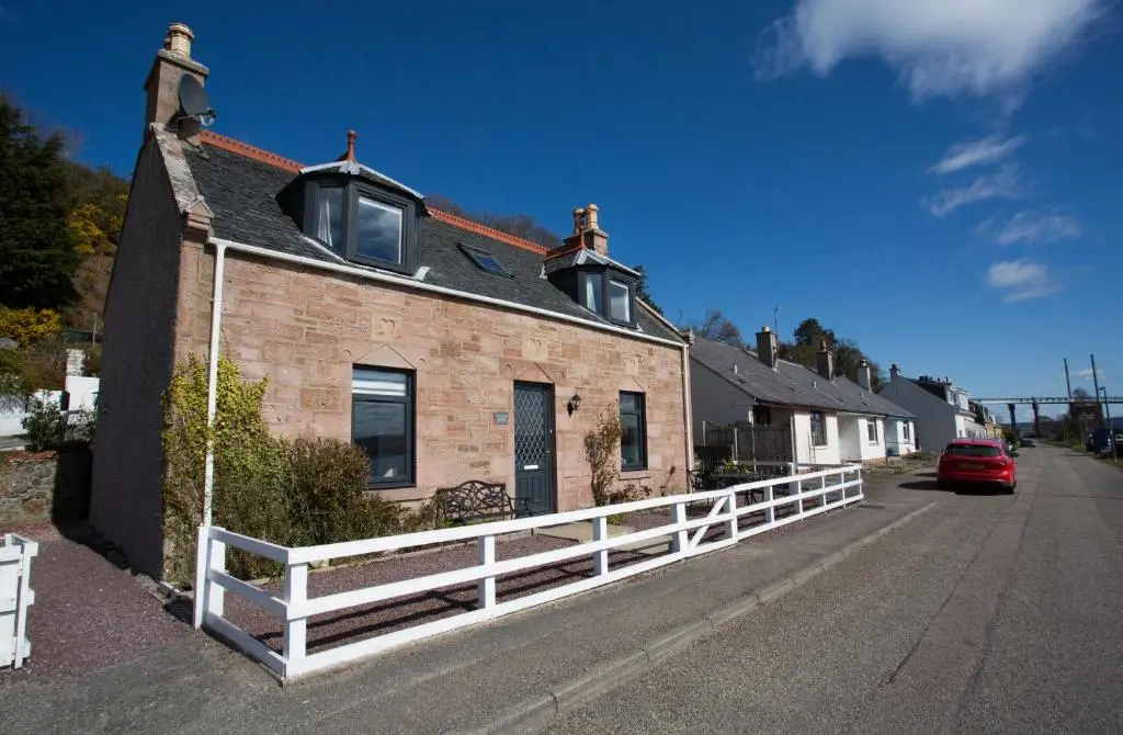 a brick house with a white fence on a street at Shore View Cottage in Inverness