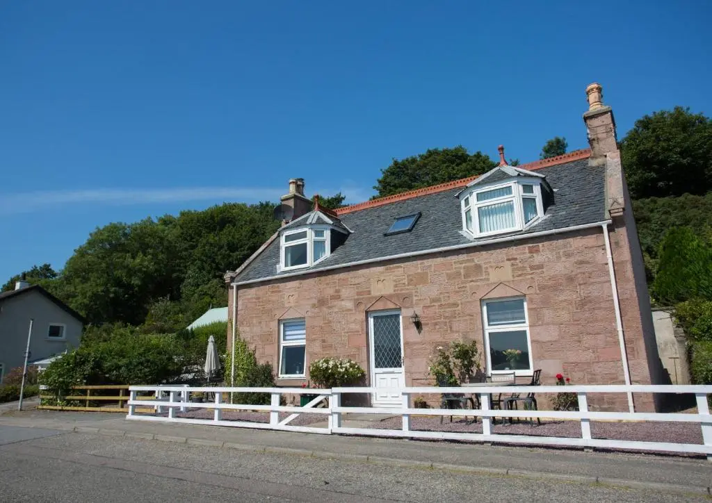 a brick house with a white fence in front of it at Shore View Cottage in Inverness