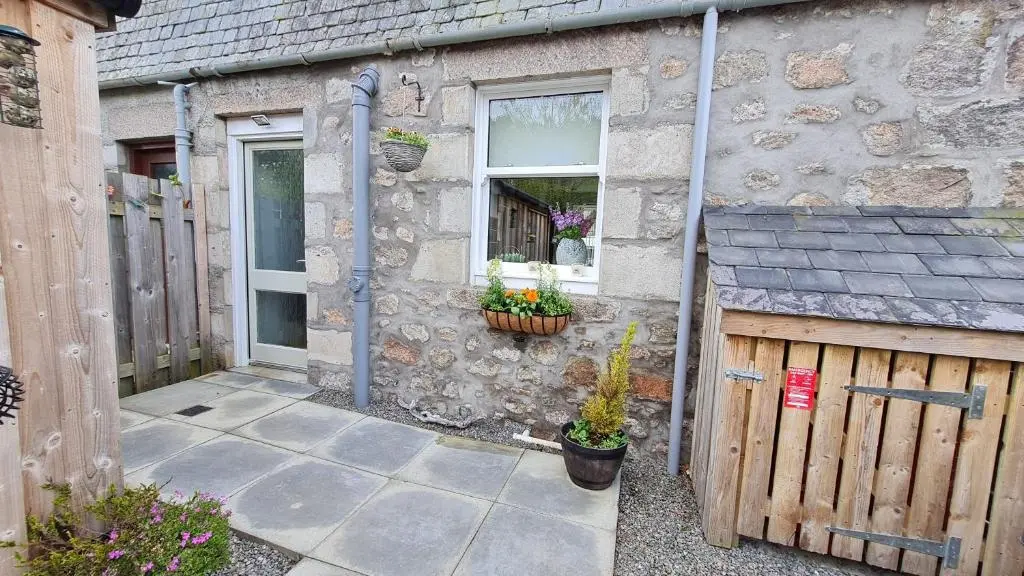 a stone house with a wooden fence and a window at Deeside Holiday Cottages in Dinnet