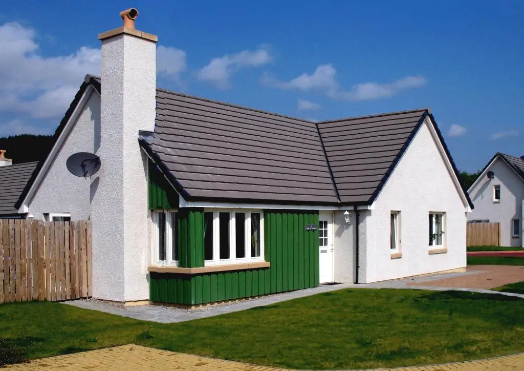 a white and green home with a black roof at Tigh na Lochan in Aviemore