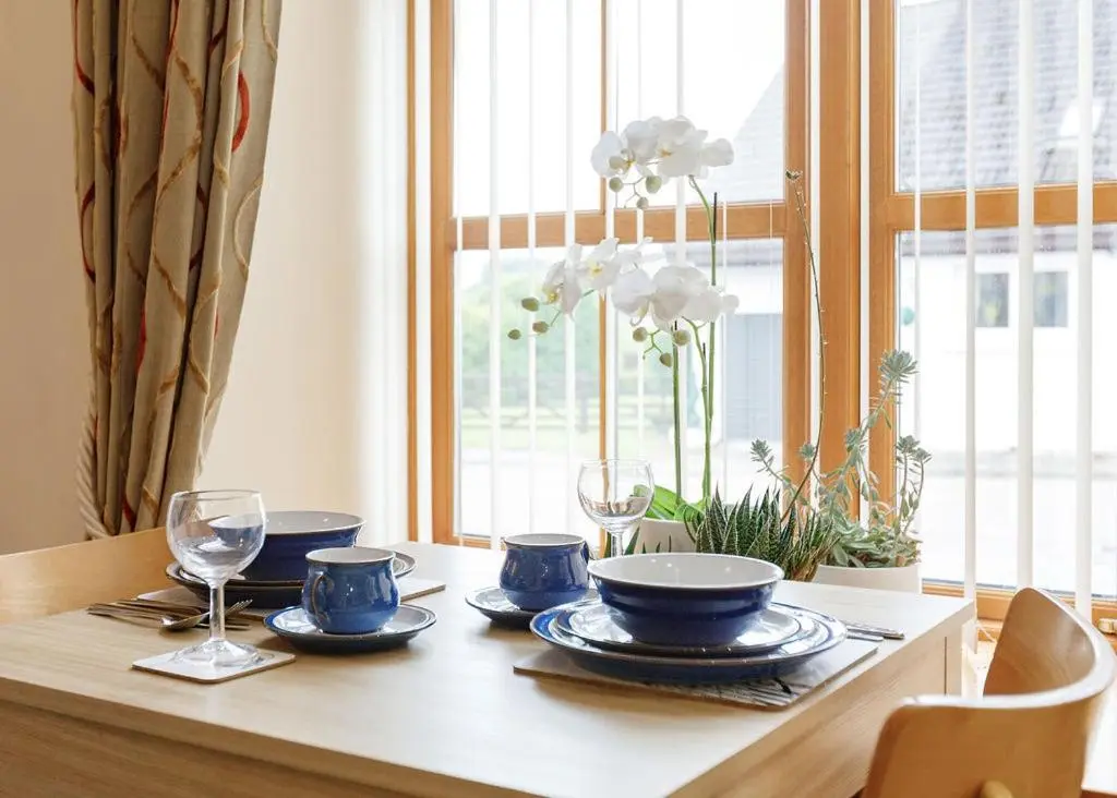 a table with blue dishes and glasses and a window at The Old Dairy in Lairg