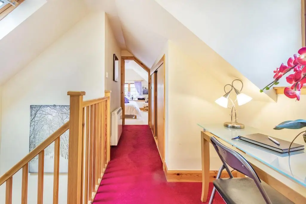 a stairway with a desk and a table with a pink carpet at Dunstaffnage Cottage in Grantown on Spey