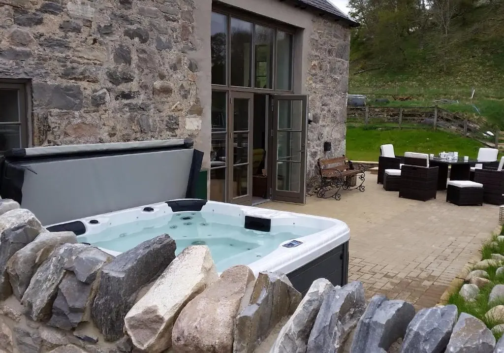 a hot tub in front of a stone house at Osprey Lodge in Kingussie