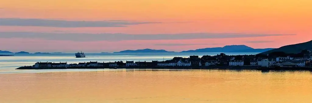 a city sitting on the water at sunset at Riverside in Ullapool