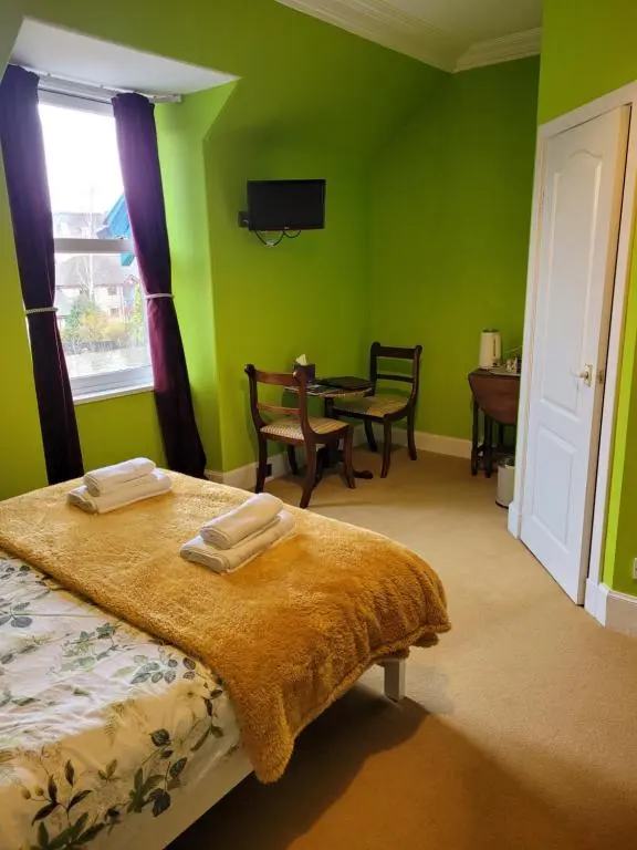 a bedroom with green walls and a bed and a table at Dunallan Guest House in Grantown on Spey