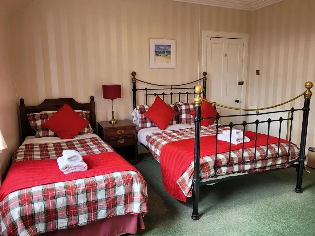 a bedroom with two beds with red and white sheets at Dunallan Guest House in Grantown on Spey