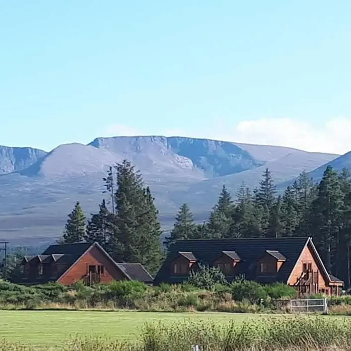 a group of houses with mountains in the background at Badaguish forest lodges and camping pods in Aviemore