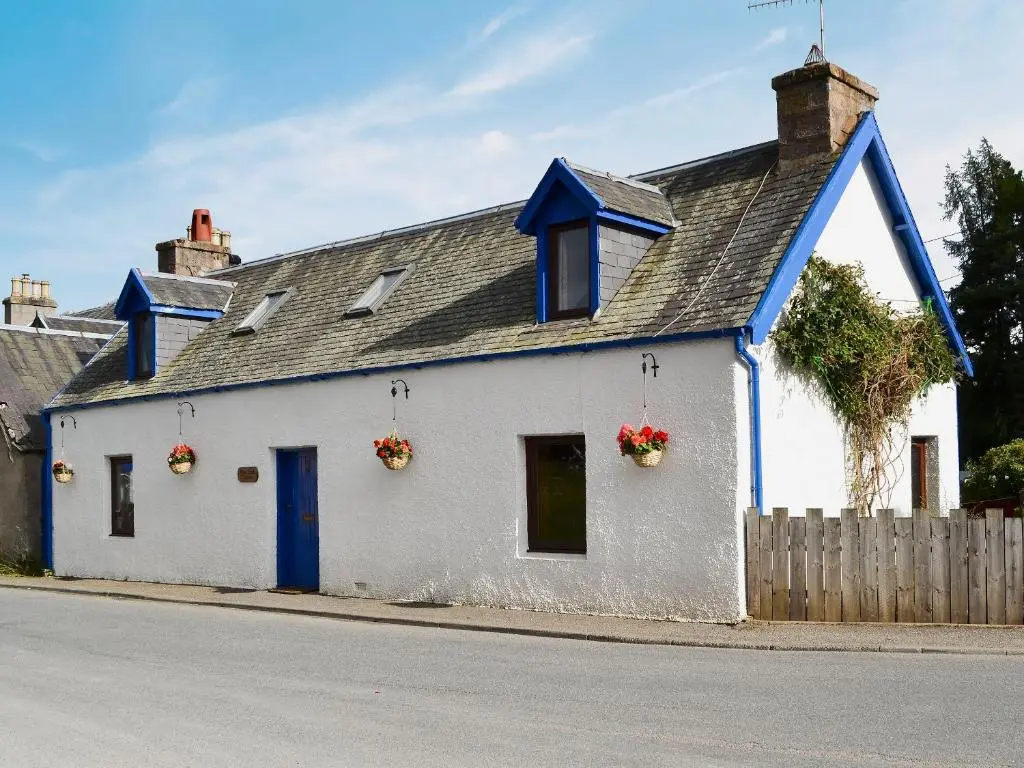 a white house with blue trim on a street at West End Cottage in Carrbridge