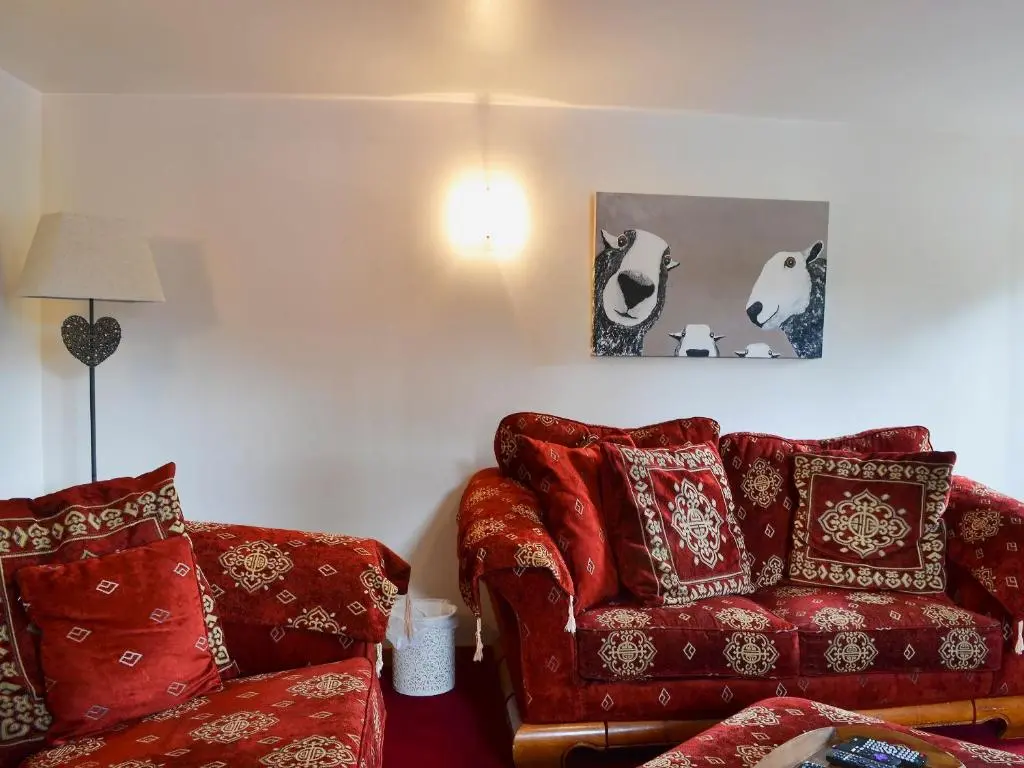 a living room with a red couch and a chair at West End Cottage in Carrbridge