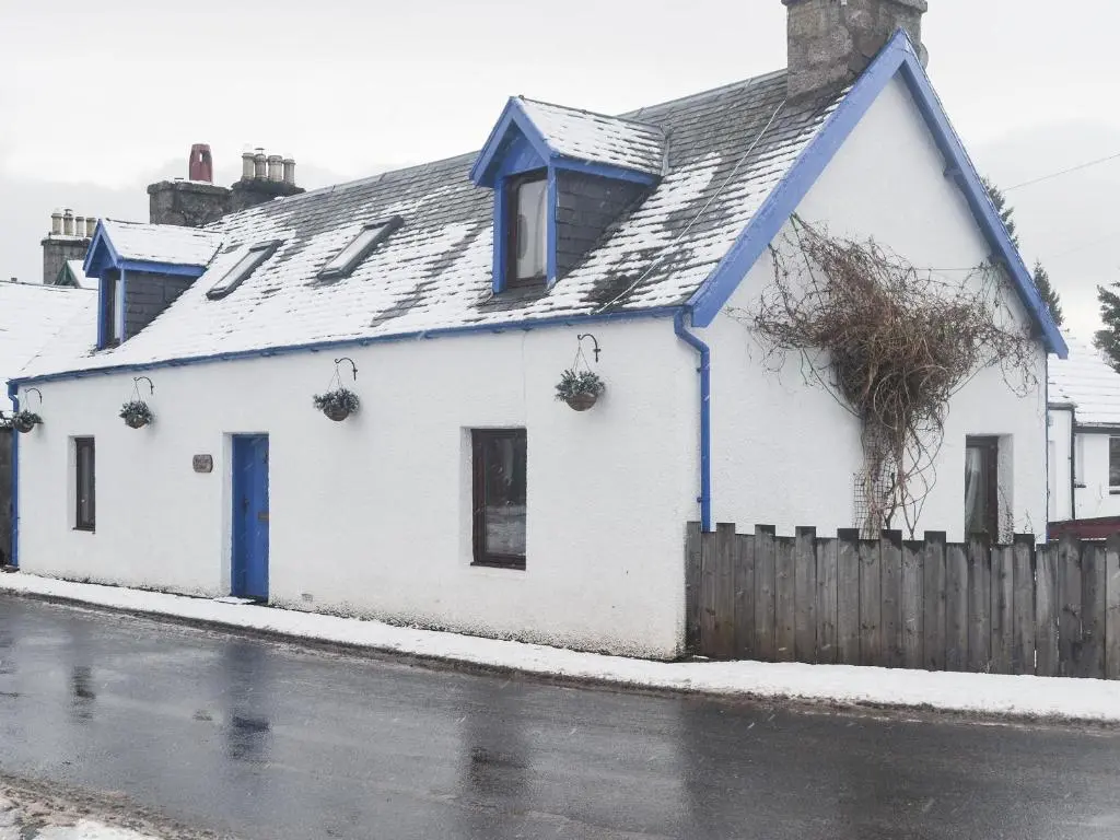a white house with a blue roof on a street at West End Cottage in Carrbridge
