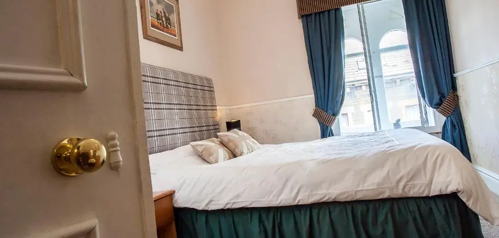 a bedroom with a bed with blue curtains and a window at Bank Guest House in Wick