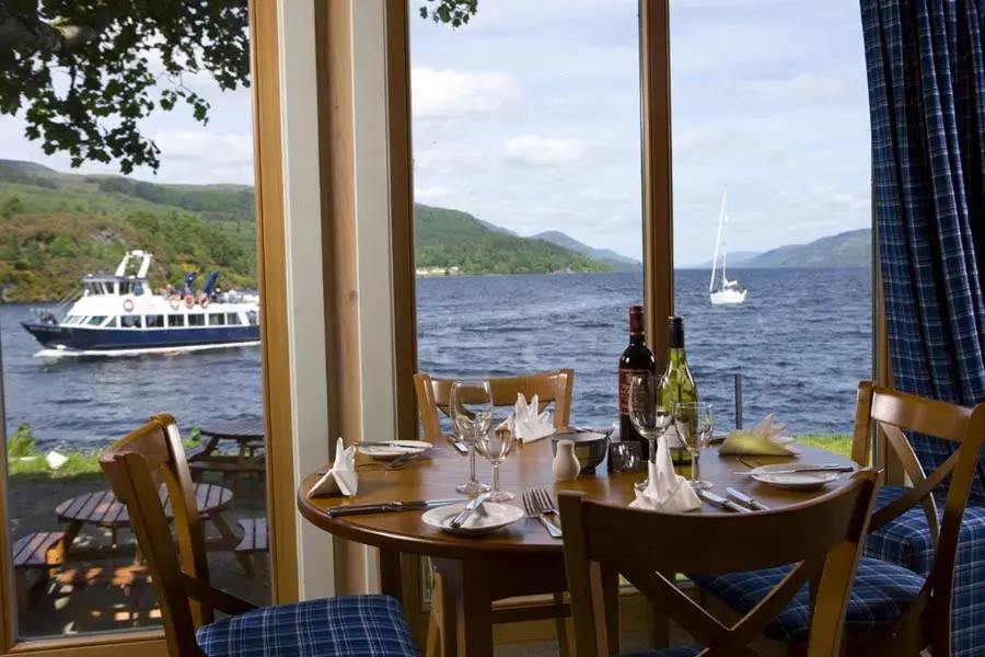 a table with wine glasses and a boat in the water at Lovat Loch Ness Apartment with private roof terrace in Fort Augustus