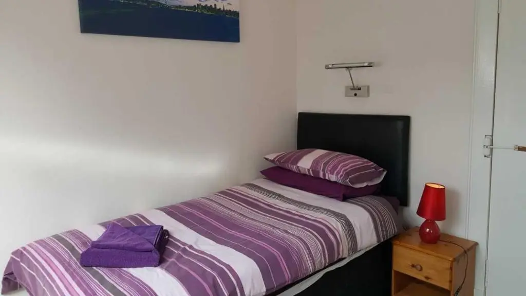a bedroom with a bed with purple sheets and a red lamp at Station View Guest House in Dyce