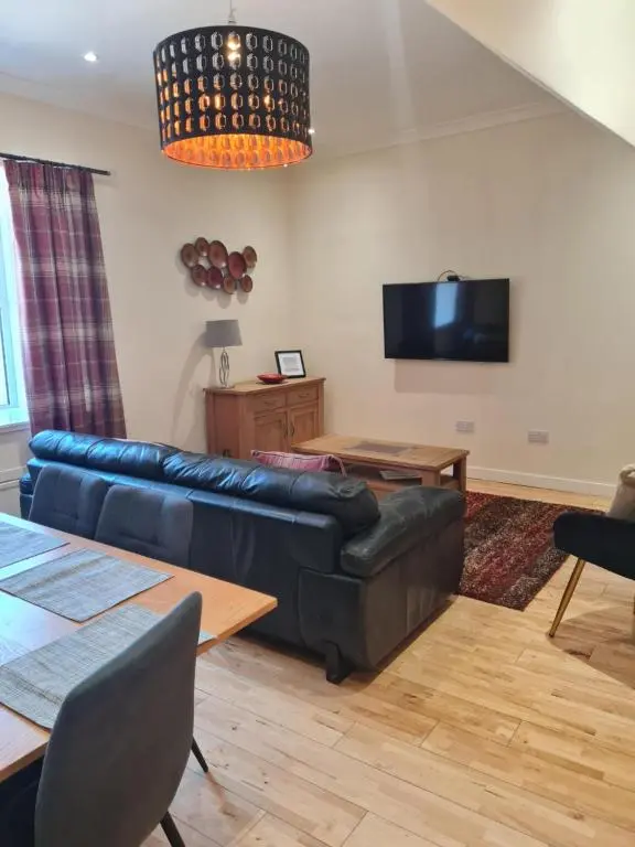 a living room with a black leather couch and a tv at Fisherman Cottage - ideal for Trades and couples part of Langley Serviced Apartments Has outside steps in Wick