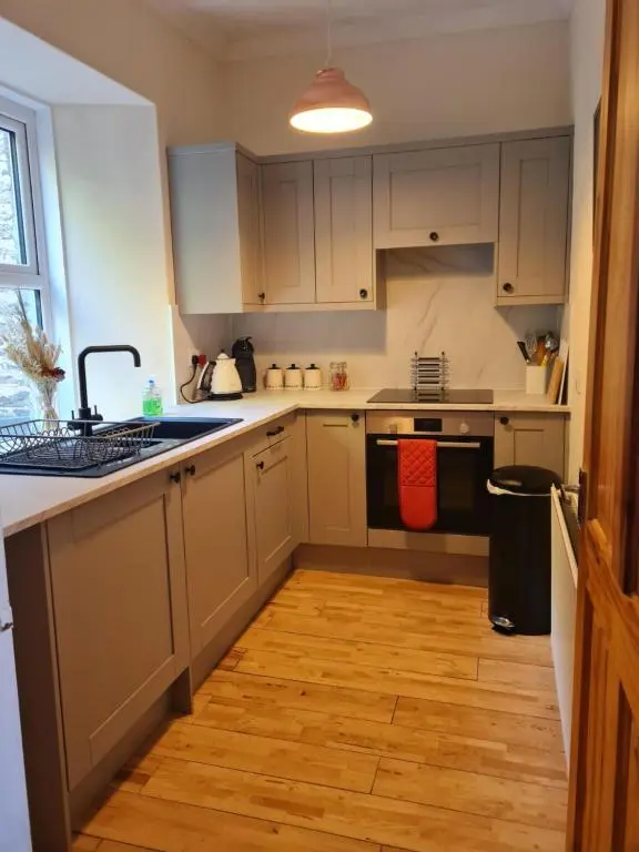 a kitchen with white cabinets and a wooden floor at Fisherman Cottage - ideal for Trades and couples part of Langley Serviced Apartments Has outside steps in Wick
