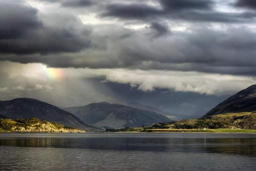 a rainbow over a body of water with mountains at Harbour House in Ullapool