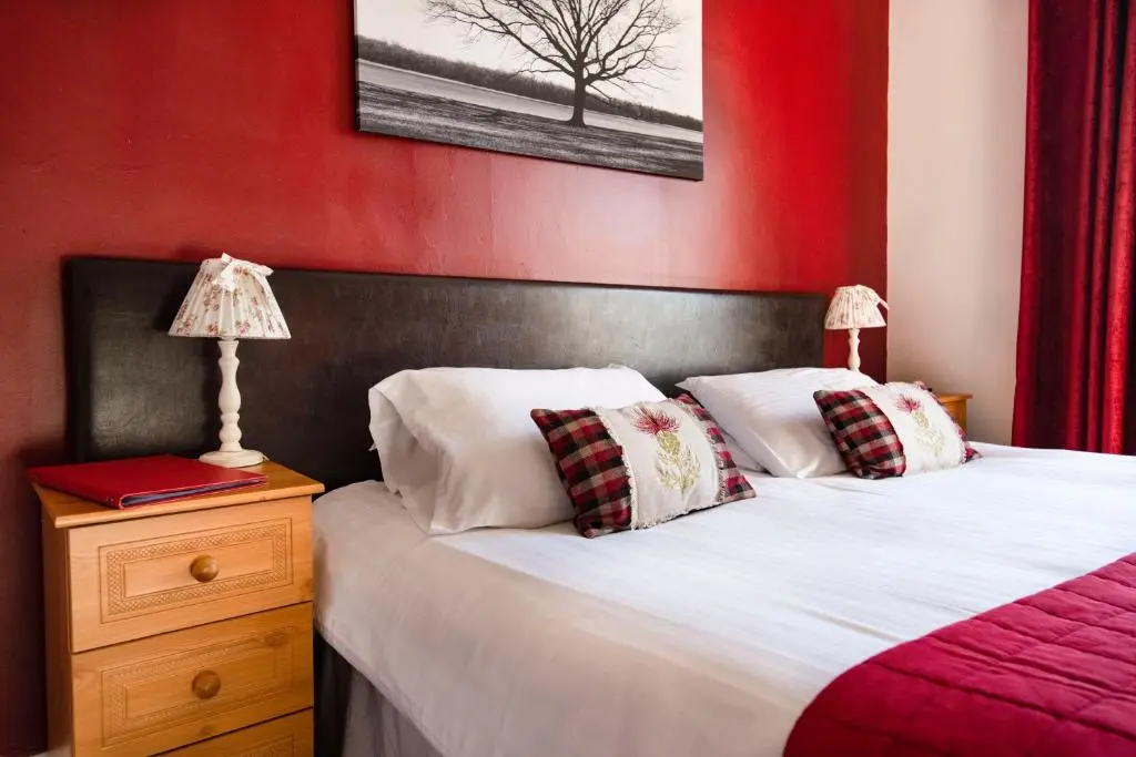a bedroom with two beds and a red wall at The Kirkmichael Hotel in Kirkmichael