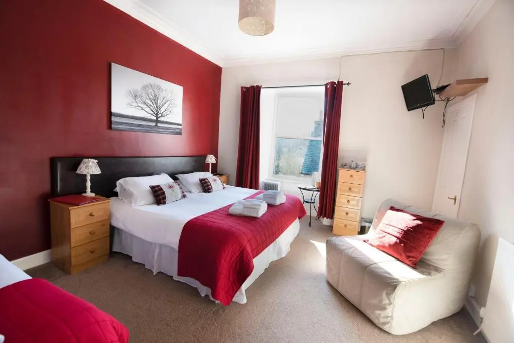 a bedroom with red walls and a bed and a chair at The Kirkmichael Hotel in Kirkmichael