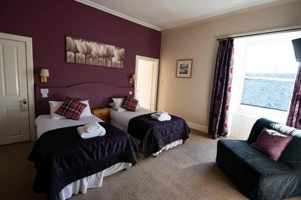 a bedroom with two beds and a chair and a window at The Kirkmichael Hotel in Kirkmichael