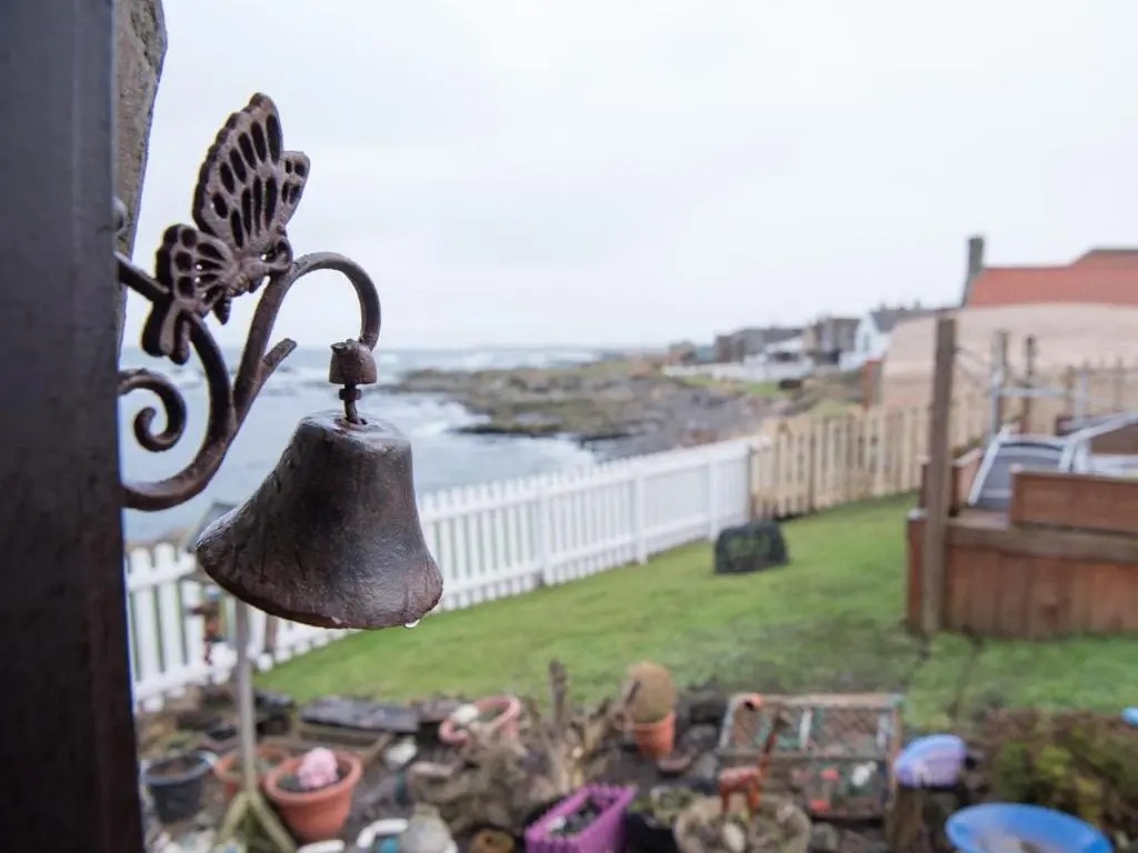 a bell on a balcony with a view of the ocean at Pew with a View - Seafront Cottages in Sandhaven