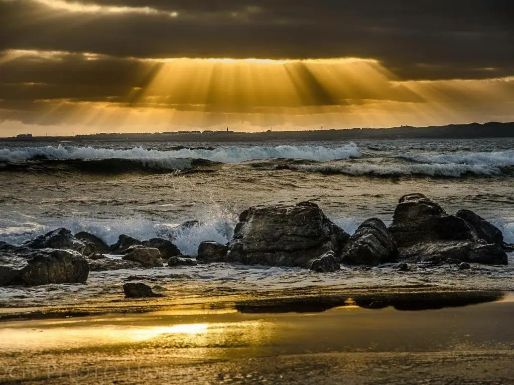 a sunset over the ocean with waves and rocks at Pew with a View - Seafront Cottages in Sandhaven