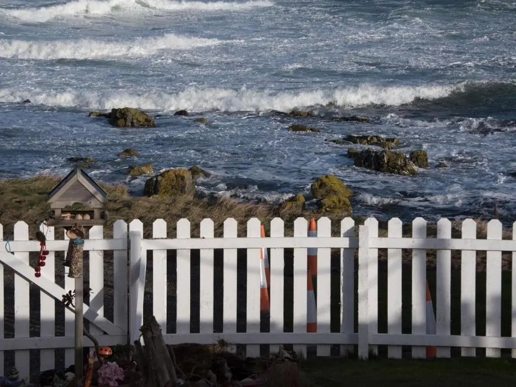 a white fence in front of the ocean at Door to the Shore - Seafront Cottages in Sandhaven