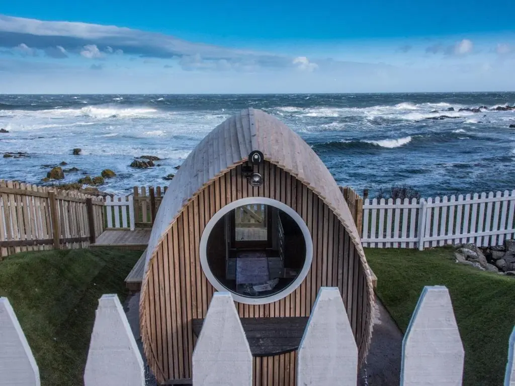 a small dog house by the ocean with a fence at Door to the Shore - Seafront Cottages in Sandhaven