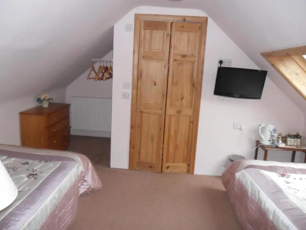 a bedroom with two beds and a door with a television at Armadale Guest House in Inverness