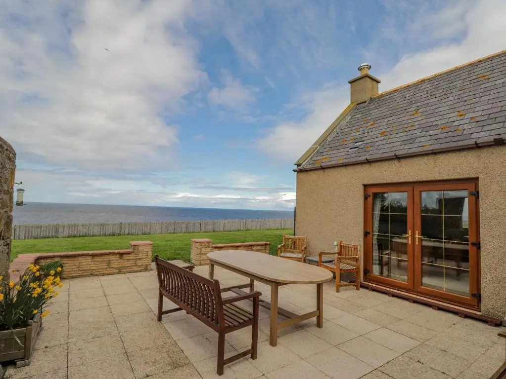 a patio with a table and chairs and the ocean at Braehead Croft in Portessie