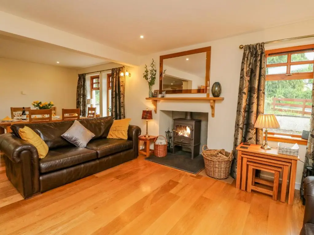 a living room with a leather couch and a fireplace at Thistle Dhu in Newtonmore