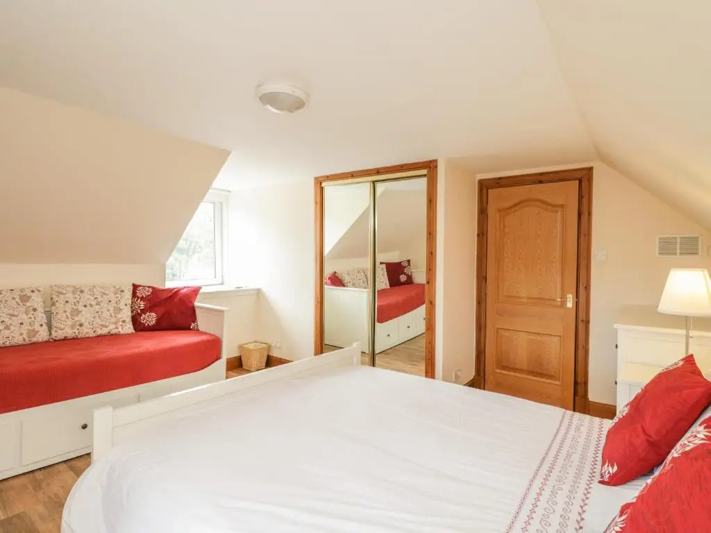 a bedroom with a white bed and a red couch at 10 Monarch Country Apartments in Newtonmore