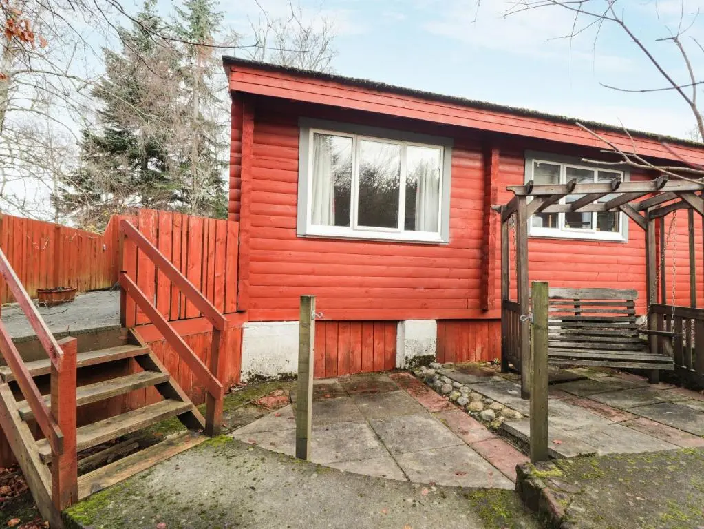 a red house with a wooden fence and stairs at Spruce Lodge in Strathpeffer