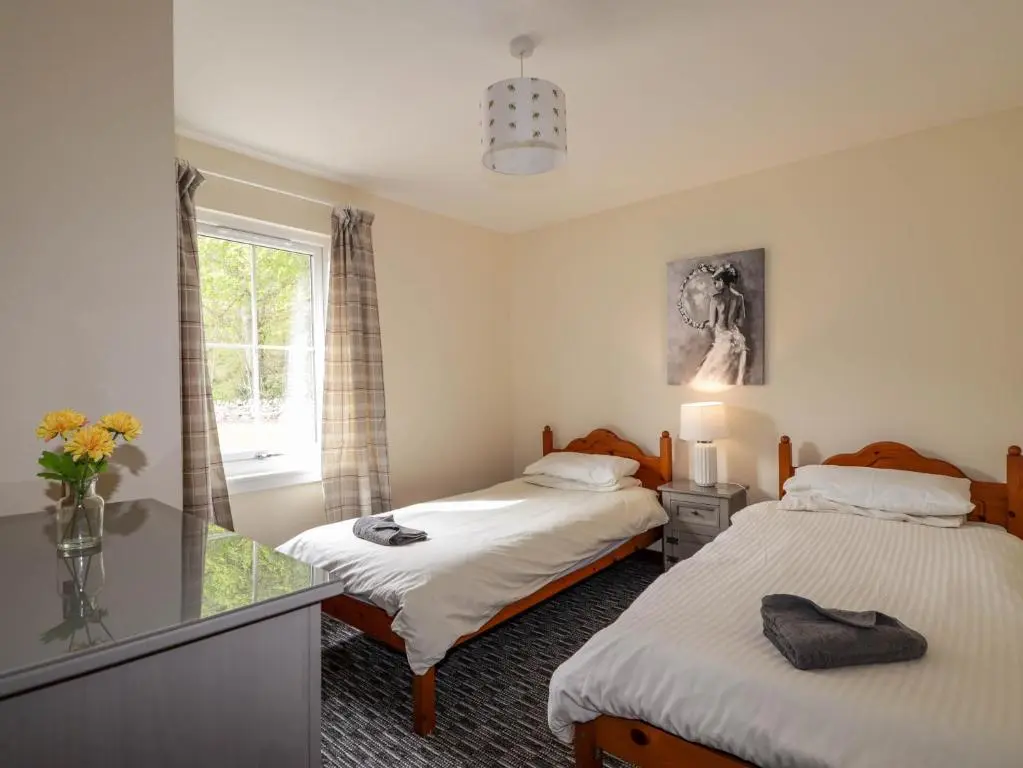 a bedroom with two beds and a window and a mirror at Stone Water Cottage in Contin