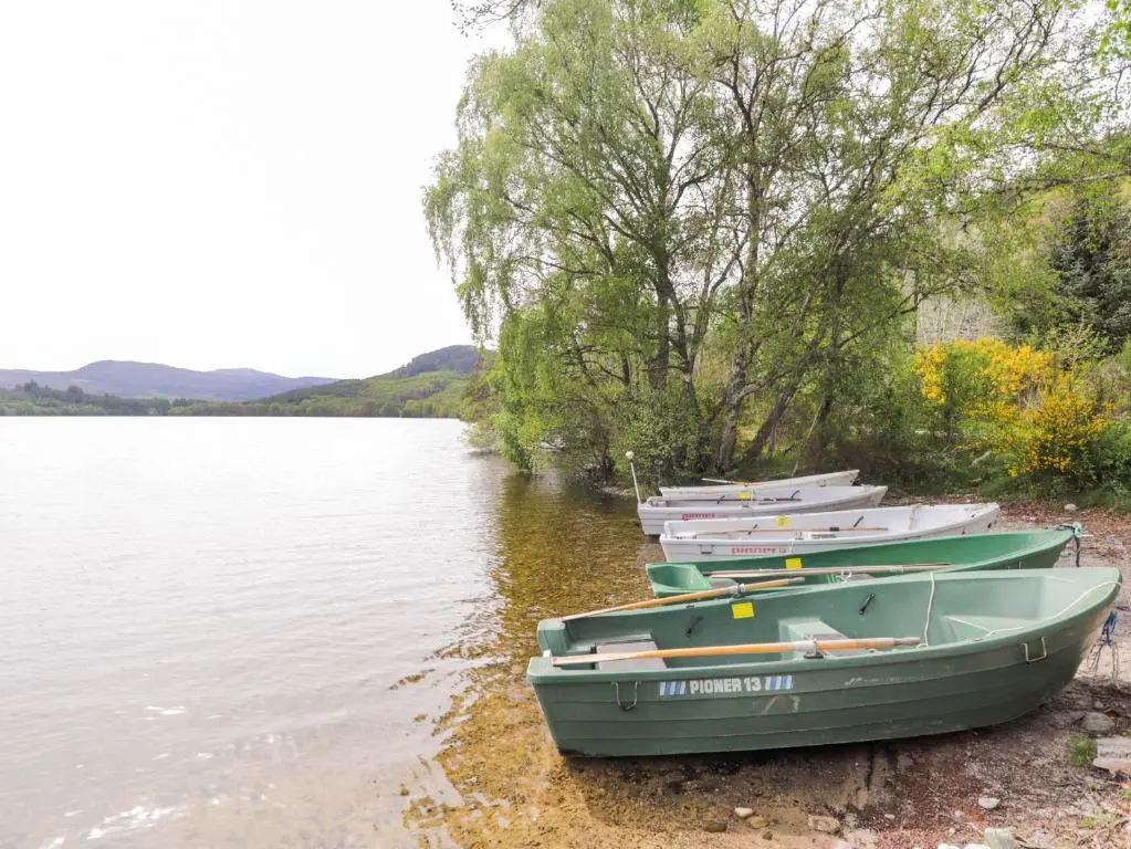 three boats sitting on the shore of a lake at Pebbles Cottage in Contin
