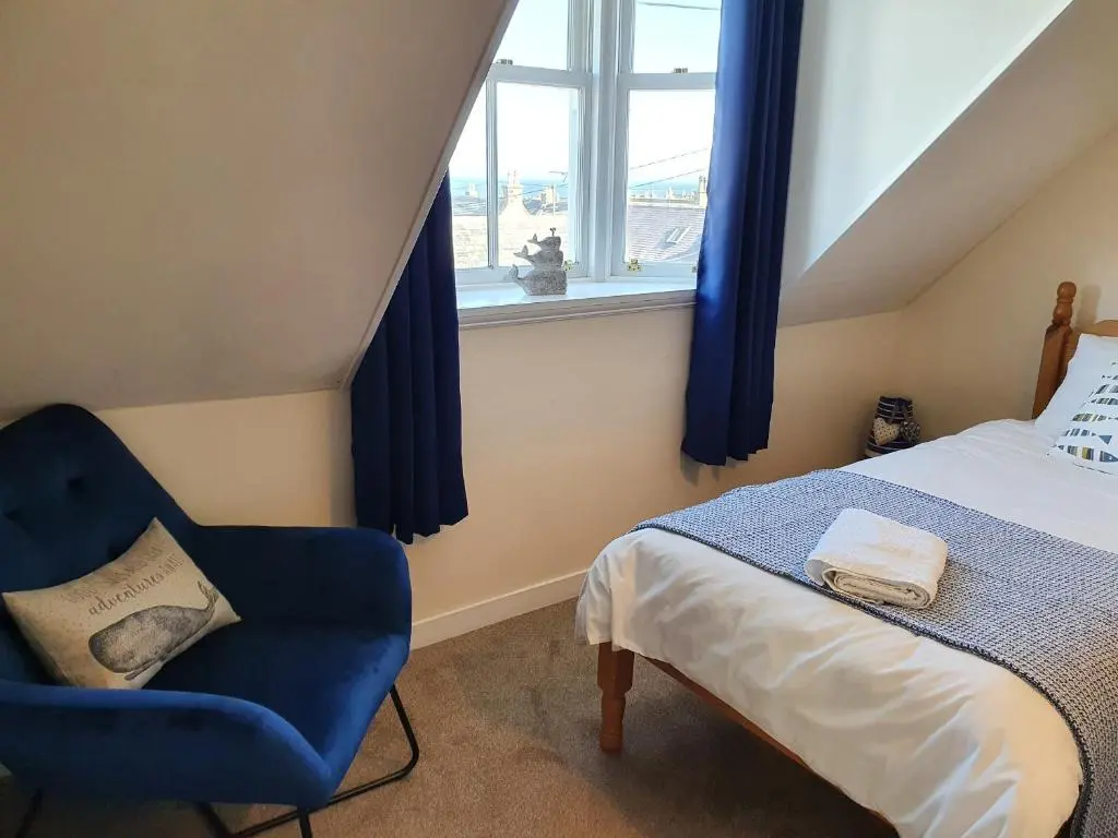 a bedroom with a bed and a blue chair and a window at Slater's in Portknockie
