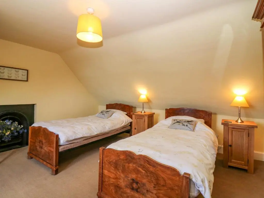 two beds in a room with two lamps and a fireplace at The West Wing in Skye of Curr
