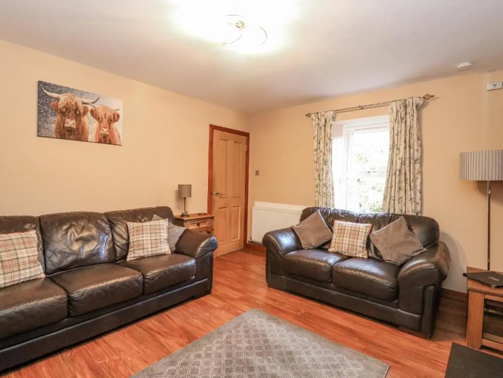 a living room with two leather couches and a window at Deskford Cottage in Balblair