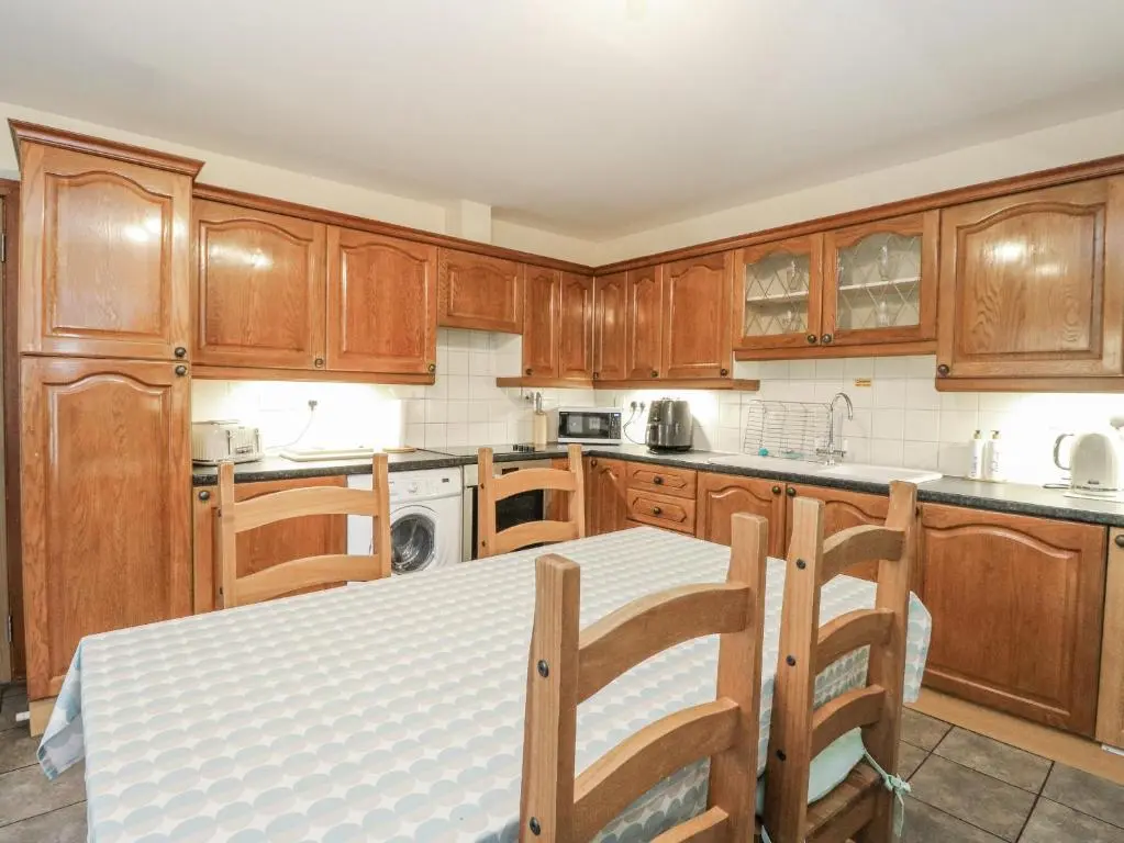 a kitchen with wooden cabinets and a table and chairs at Deskford Cottage in Balblair