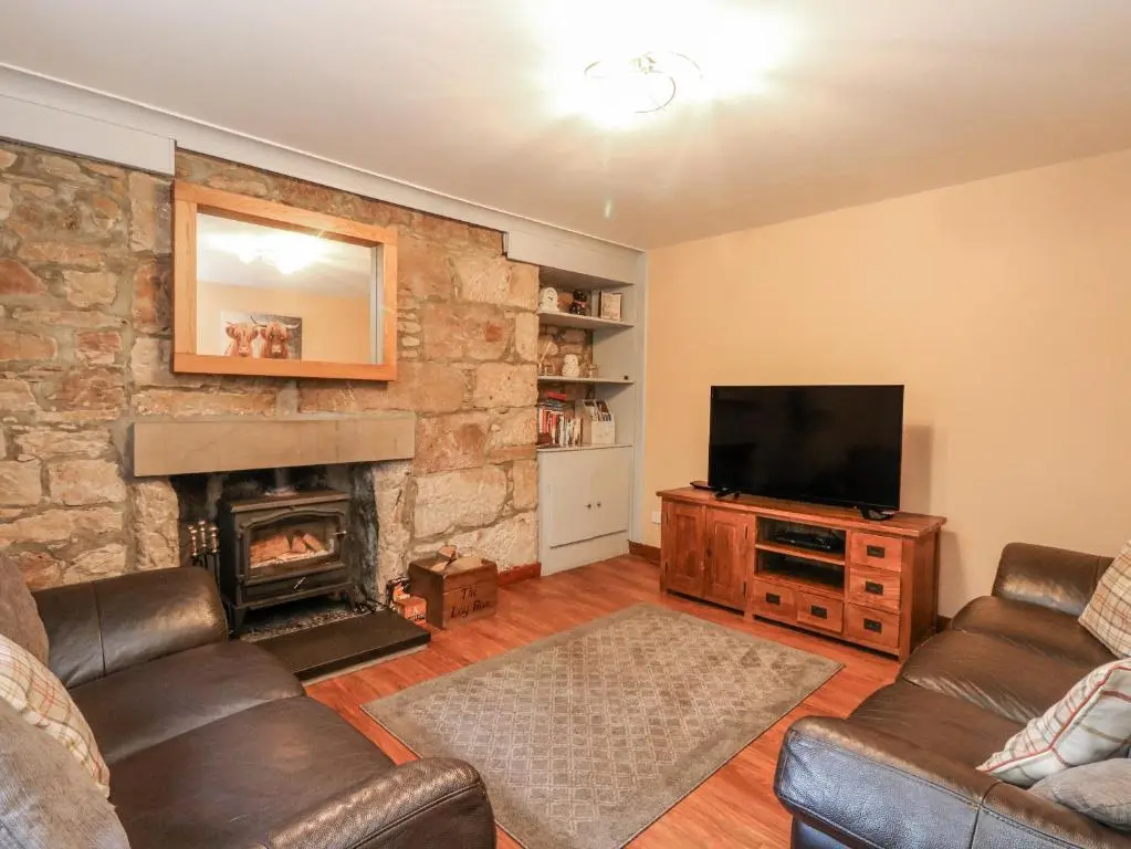 a living room with a fireplace and a television at Deskford Cottage in Balblair