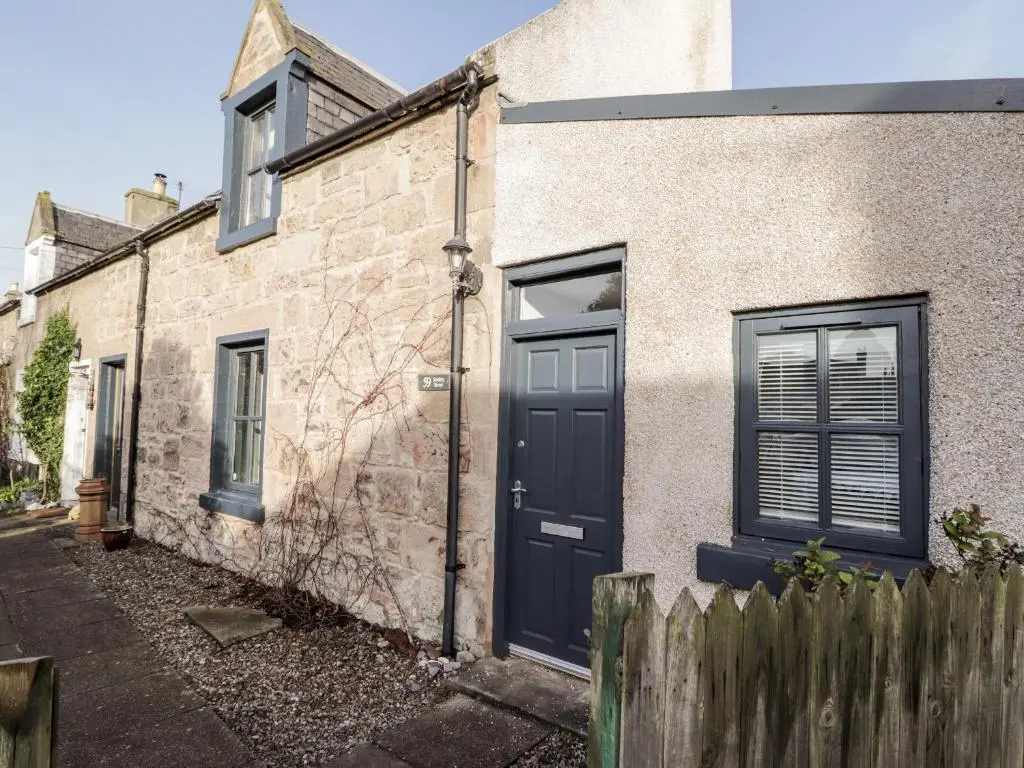 a brick house with a black door and a fence at 59 Society Street in Nairn