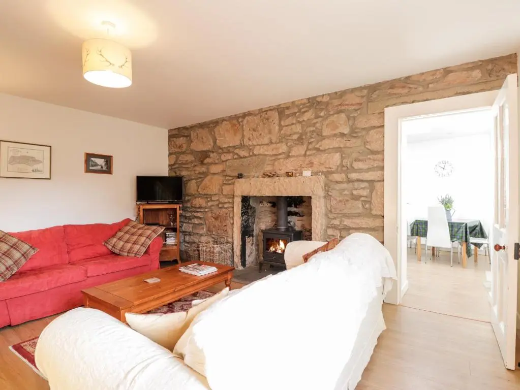 a living room with a red couch and a stone wall at 59 Society Street in Nairn