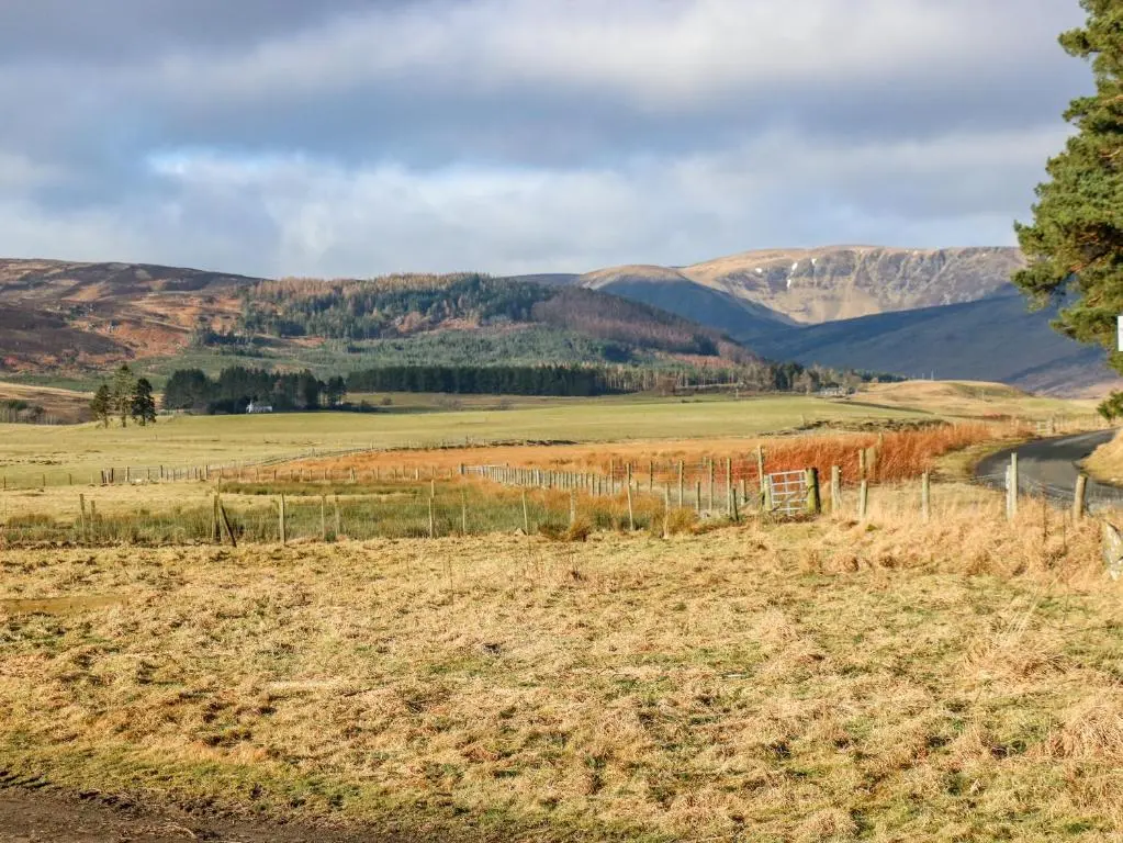 a field with a fence and mountains in the background at White Hillocks Cottage in Inchmill