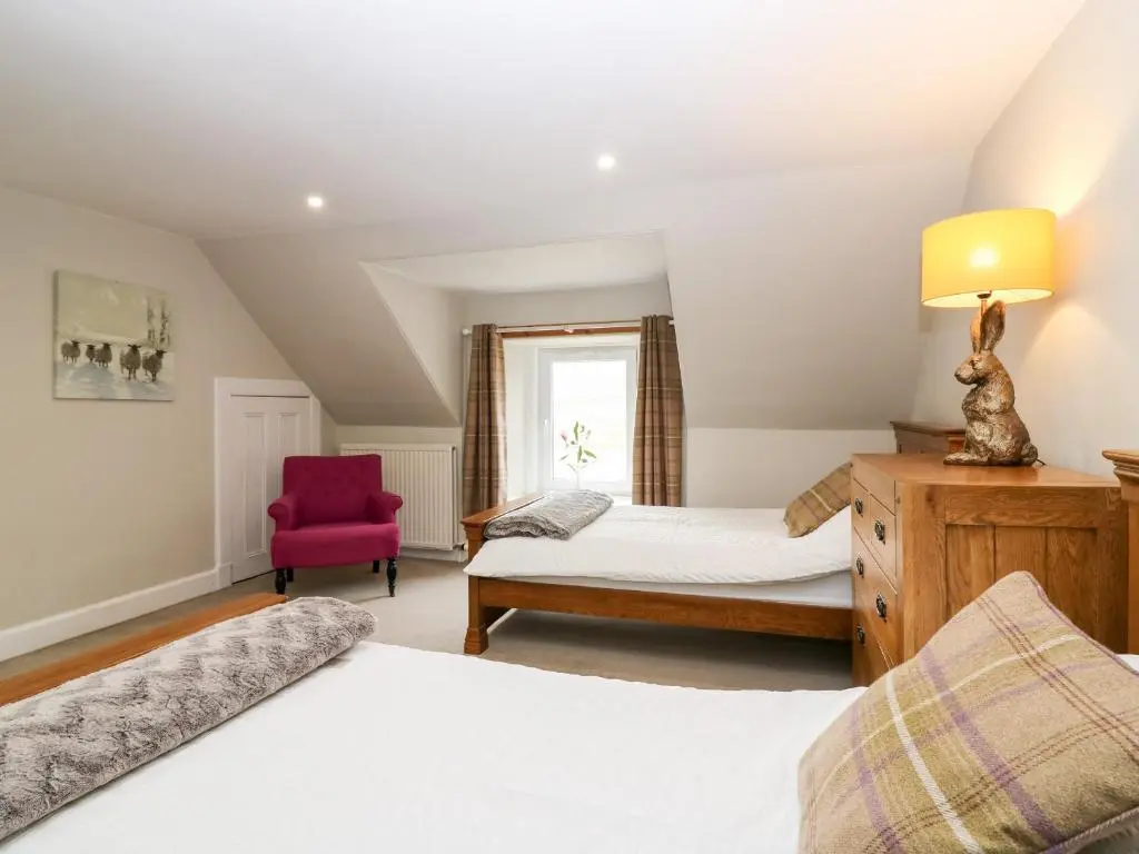 a bedroom with two beds and a red chair at White Hillocks Farm House in Inchmill
