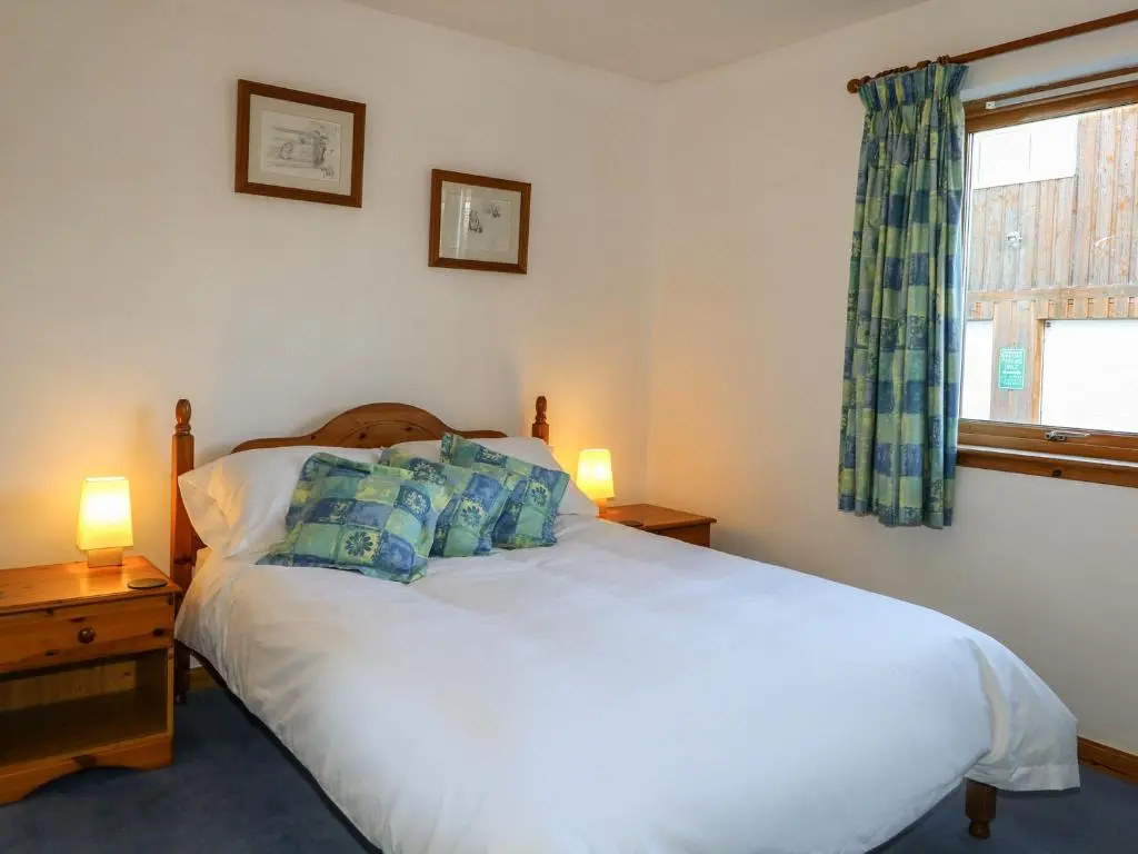 a bedroom with a bed with blue pillows and a window at Corriemhor Beag in Cromdale