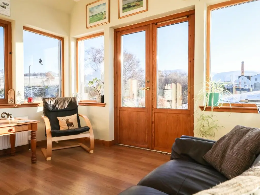 a living room with a couch and a chair and windows at Corriemhor Beag in Cromdale